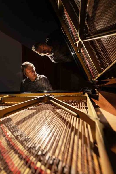 Ein Mann spielt konzentriert Klavier, das Innere des Flügels ist im Vordergrund zu sehen. Der Raum ist dunkel, der Fokus liegt auf dem Musiker., © Kulturhaus Schwanen