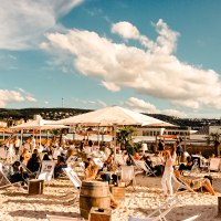 Strandbar mit Liegest&uuml;hlen und Sonnenschirmen, umgeben von Palmen. Menschen entspannen sich unter blauem Himmel mit Wolken., &copy; Sky Beach