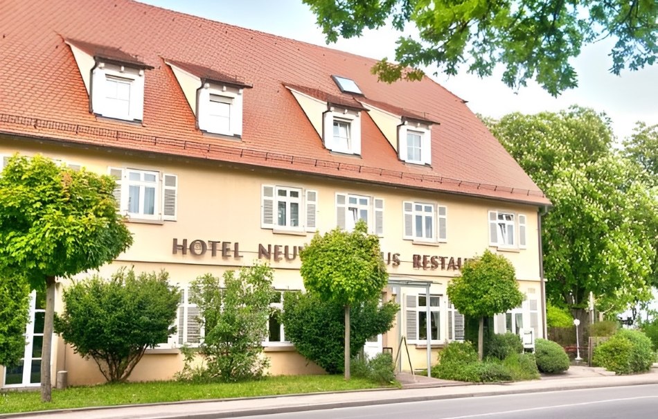 Ein Hotel mit rotem Dach und mehreren Fenstern, umgeben von grünen Bäumen und Sträuchern, an einer Straße gelegen., © Hotel Neuwirtshaus