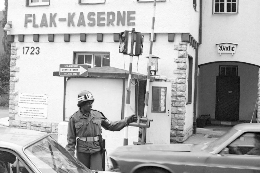 Ein Soldat in Uniform dirigiert den Verkehr vor der Flak-Kaserne. Ein Schild weist auf die USAREUR License Station hin. Autos fahren vorbei., &copy; Ludwigsburg Museum
