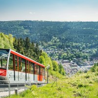 Die Sommerbergbahn in Bad Wildbad f&auml;hrt durch eine gr&uuml;ne Landschaft. Im Hintergrund ist die Stadt und ein bewaldeter H&uuml;gel zu sehen., &copy; Touristik Bad Wildbad