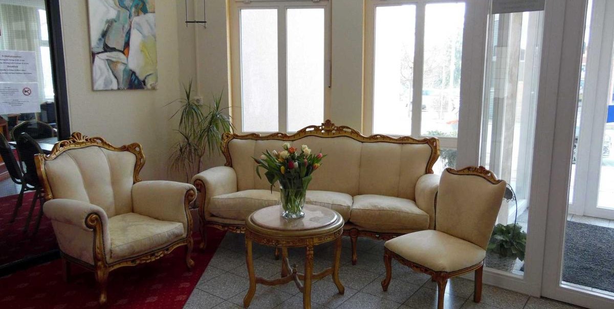 Elegante Lobby mit antiken Möbeln: ein Sofa, zwei Sessel und ein Stuhl um einen Tisch mit Blumenstrauß. Kunstwerk an der Wand, große Fenster im Hintergrund., © Hotel Arcis Elegante Lobby mit antiken Möbeln: ein Sofa, zwei Sessel und ein Stuhl um einen Tisch mit Blumenstrauß. Kunstwerk an der Wand, große Fenster im Hintergrund., © Hotel Arcis