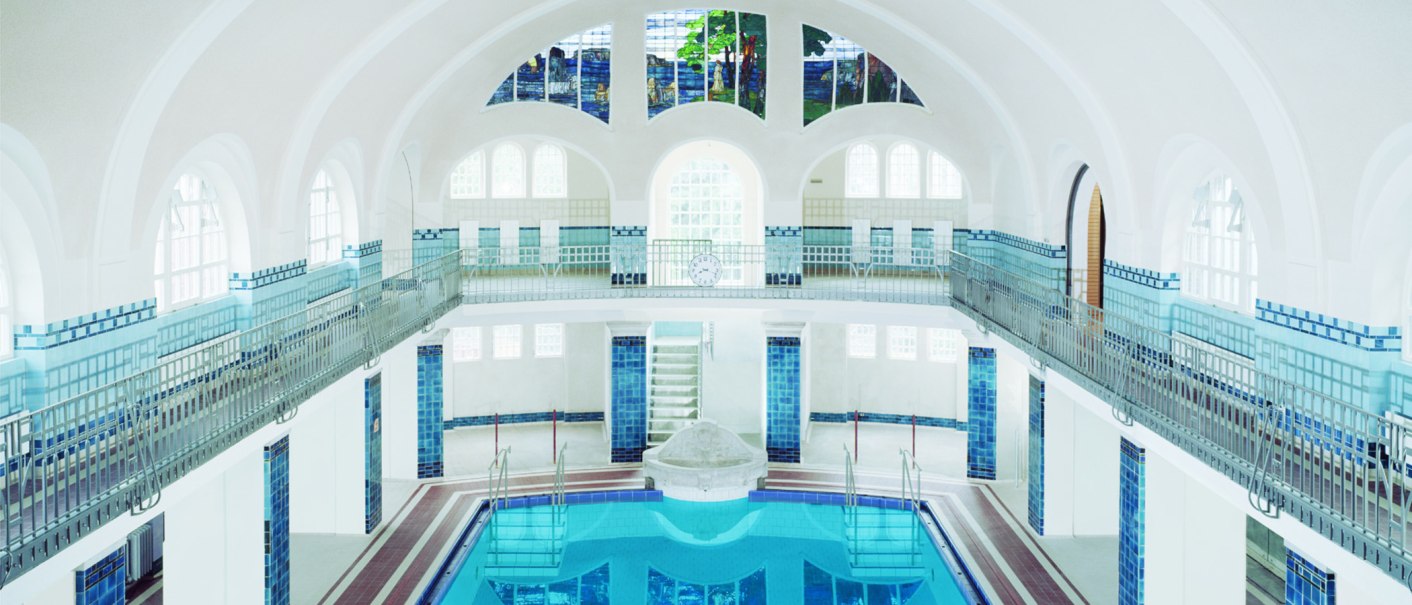 Innenansicht des Merkel'schen Schwimmbads in Esslingen. Das Becken ist von blauen Fliesen umgeben, mit hohen Fenstern und einem kunstvollen Glasfenster., © Esslinger Stadtmarketing & Tourismus GmbH