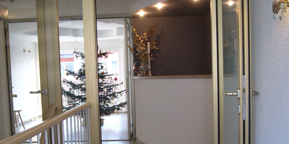 Eingangsbereich mit Glastüren, einem dekorierten Weihnachtsbaum und einer beleuchteten Ecke mit Kerzen und Pflanzen., © Hotelmärchen