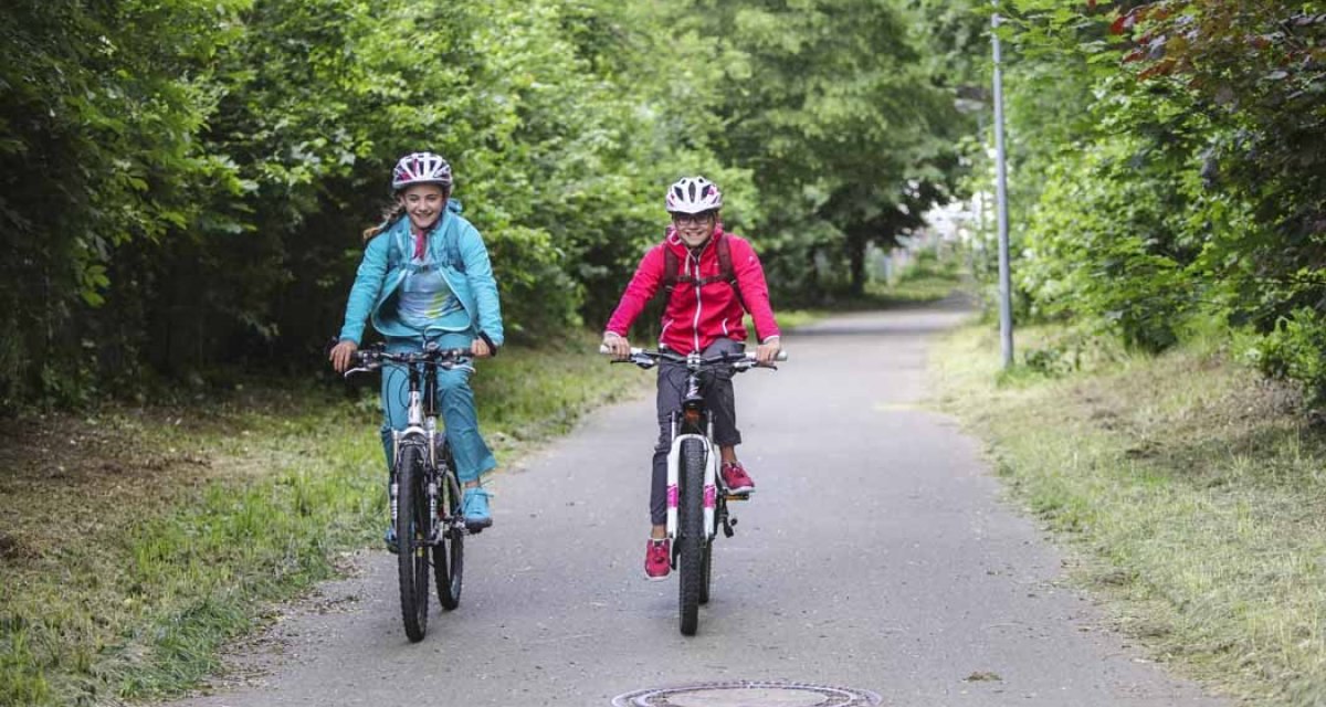 Zwei Kinder fahren auf einem Fahrradweg durch eine grüne Allee. Sie tragen Helme und bunte Kleidung. Der Weg ist von Bäumen gesäumt., © Schwäbische Alb Tourismusverband e.V. Zwei Kinder fahren auf einem Fahrradweg durch eine grüne Allee. Sie tragen Helme und bunte Kleidung. Der Weg ist von Bäumen gesäumt., © Schwäbische Alb Tourismusverband e.V.