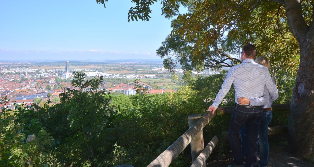 Ein Paar steht an einem Geländer und schaut auf das Remstal. Im Hintergrund ist eine Stadt mit einem hohen Gebäude zu sehen, umgeben von Bäumen., © Remstal Tourismus e.V. Ein Paar steht an einem Geländer und schaut auf das Remstal. Im Hintergrund ist eine Stadt mit einem hohen Gebäude zu sehen, umgeben von Bäumen., © Remstal Tourismus e.V.
