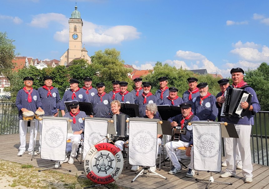 Eine M&auml;nnergruppe in Matrosenuniformen mit Instrumenten posiert vor einer Kirche. Im Hintergrund sind B&auml;ume und ein Kirchturm zu sehen., &copy; Neckar-Knurrh&auml;hne