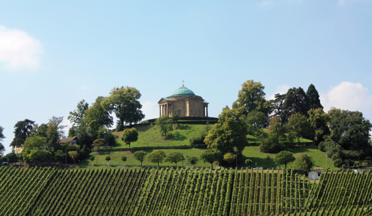 Die Grabkapelle auf dem Württemberg thront auf einem Hügel, umgeben von grünen Weinbergen und Bäumen unter einem blauen Himmel., © Stuttgart-Marketing GmbH Die Grabkapelle auf dem Württemberg thront auf einem Hügel, umgeben von grünen Weinbergen und Bäumen unter einem blauen Himmel., © Stuttgart-Marketing GmbH