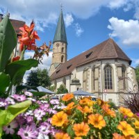 Kirche mit Kirchturm vor blauem Himmel mit weißen Wolken, davor bunte Sommerblumen, © Petra Natzkowski