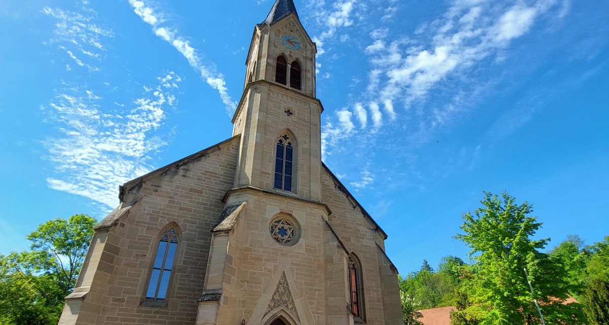 Die Evangelische Schlosskirche Remseck-Hochberg vor blauem Himmel mit dekorativen Wolken. Der Kirchturm ragt in die Höhe, umgeben von Bäumen. Die Evangelische Schlosskirche Remseck-Hochberg vor blauem Himmel mit dekorativen Wolken. Der Kirchturm ragt in die Höhe, umgeben von Bäumen.
