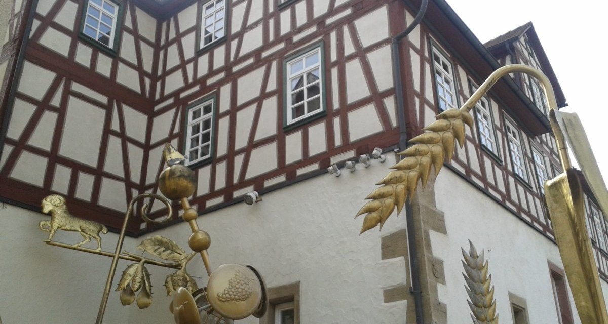 Fachwerkhaus mit goldener Skulptur im Vordergrund, die landwirtschaftliche Symbole wie Getreide und Tiere darstellt., &copy; Natur.Nah. Sch&ouml;nbuch & Heckeng&auml;u