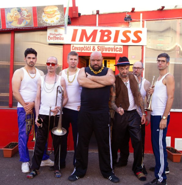 Sieben Männer in sportlicher Kleidung posieren vor einem Imbiss mit der Aufschrift 'IMBISS Čevapčići & Šljivovica'., © Interessengemeinschaft Kultur Sindelfingen / Böblingen e.V.