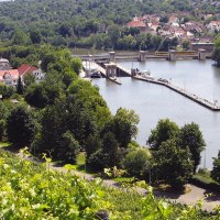 Blick auf den Neckar mit Schleuse, umgeben von Häusern, Bäumen und Weinbergen. Im Hintergrund eine bewaldete Hügellandschaft., © Stuttgart-Marketing GmbH Blick auf den Neckar mit Schleuse, umgeben von Häusern, Bäumen und Weinbergen. Im Hintergrund eine bewaldete Hügellandschaft., © Stuttgart-Marketing GmbH