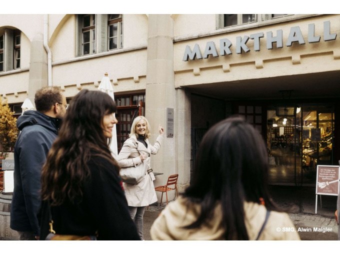 Gruppe vor der Markthalle, eine Frau zeigt l&auml;chelnd auf das Schild. Menschen in Freizeitkleidung, Eingang im Hintergrund., &copy; Stuttgart Marketing GmbH