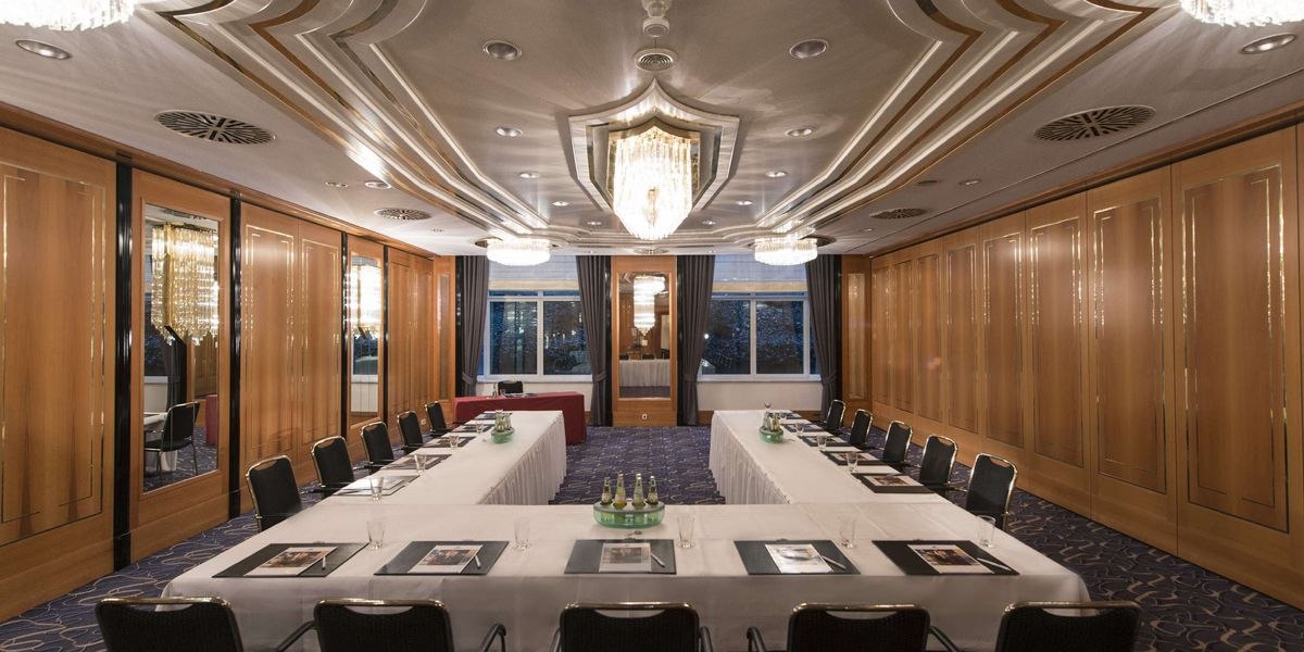 Eleganter Tagungsraum mit U-förmiger Tischanordnung, Kronleuchtern und Holzwänden. Der Raum ist für eine Konferenz vorbereitet., © Maritim Hotelgesellschaft mbH