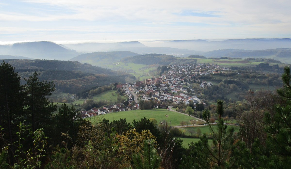 Panoramablick auf ein Dorf in einer hügeligen Landschaft, umgeben von Wäldern und Feldern, unter einem bewölkten Himmel., © Foto: Frieder Kopper