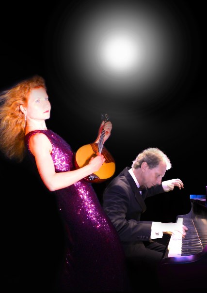 Eine Frau in einem glitzernden Kleid spielt eine Domra, während ein Mann im Anzug Klavier spielt. Der Hintergrund ist schwarz mit einem Lichtschein., © DomraPiano