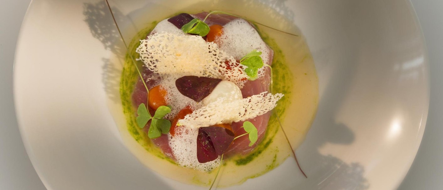 Ein kunstvoll angerichtetes Gourmetgericht mit Schaum, Kräutern und knusprigen Elementen auf einem Teller., © Restaurant Bachofer