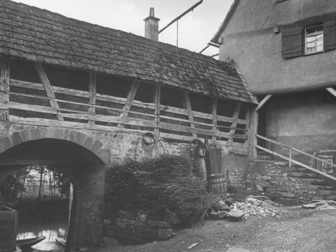 Altes Fachwerkgebäude mit Steinmauer und Holzfassaden in Waiblingen, umgeben von Fässern und Zweigen. Historische Architektur zur NS-Zeit., © WTM GmbH Waiblingen Altes Fachwerkgebäude mit Steinmauer und Holzfassaden in Waiblingen, umgeben von Fässern und Zweigen. Historische Architektur zur NS-Zeit., © WTM GmbH Waiblingen
