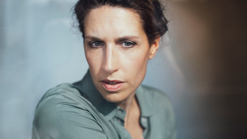 Porträt einer Frau mit nachdenklichem Ausdruck, die ein grünes Hemd trägt. Der Hintergrund ist unscharf, was den Fokus auf ihr Gesicht lenkt., © Konzertkreis Triangel Compagnia Compostelli e.V.