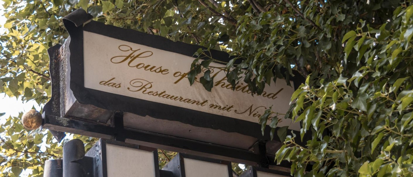 Ein Schild mit der Aufschrift 'House of Thailand, das Restaurant mit Niveau', umgeben von grünen Blättern., © Stuttgart Marketing GmbH, Sarah Schmid Ein Schild mit der Aufschrift 'House of Thailand, das Restaurant mit Niveau', umgeben von grünen Blättern., © Stuttgart Marketing GmbH, Sarah Schmid