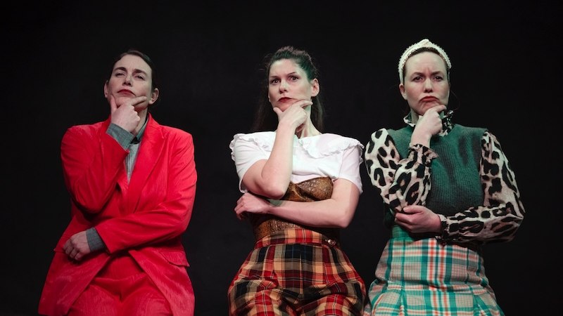 Drei Frauen in verschiedenen Outfits sitzen nachdenklich auf einer Bank vor schwarzem Hintergrund., © Kulturhaus Schwanen