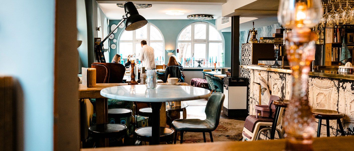 Gem&uuml;tliches Caf&eacute; mit stilvoller Einrichtung, runden Tischen und St&uuml;hlen. Menschen sitzen und unterhalten sich. Gro&szlig;e Fenster lassen Licht herein., &copy; Stuttgart-Marketing GmbH, Sarah Schmid