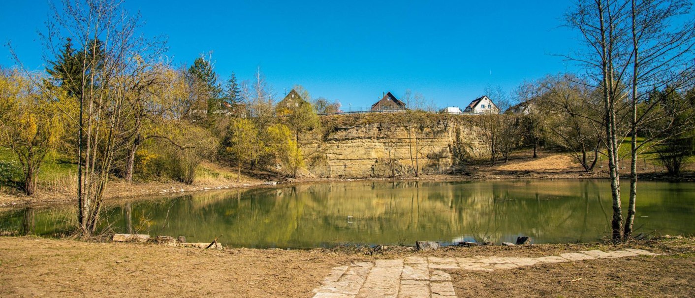 Ein idyllischer See mit Bäumen und Häusern im Hintergrund, unter einem klaren blauen Himmel. Die Landschaft spiegelt sich im Wasser., © Stuttgart-Marketing GmbH, Sarah Schmid Ein idyllischer See mit Bäumen und Häusern im Hintergrund, unter einem klaren blauen Himmel. Die Landschaft spiegelt sich im Wasser., © Stuttgart-Marketing GmbH, Sarah Schmid