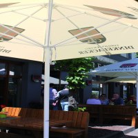 Außenbereich der Brauereigaststätte Dinkelacker mit Holzbänken und Sonnenschirmen. Gäste sitzen im Schatten und genießen das Wetter., © Stuttgart-Marketing GmbH