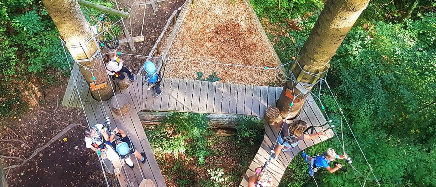 Luftaufnahme von Menschen auf Plattformen im Kletterwald, umgeben von Bäumen. Sie tragen Sicherheitsausrüstung und Helme., © SKYPARK – epia-store.de GbR Luftaufnahme von Menschen auf Plattformen im Kletterwald, umgeben von Bäumen. Sie tragen Sicherheitsausrüstung und Helme., © SKYPARK – epia-store.de GbR