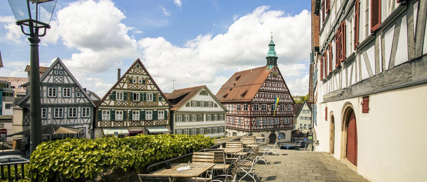 Blick auf historische Fachwerkh&auml;user in Backnang. Im Vordergrund leere Sitzpl&auml;tze, im Hintergrund ein blauer Himmel mit Wolken., &copy; SMG, Sarah Schmid