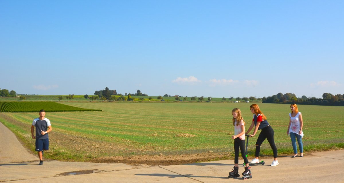 Menschen auf einem Feldweg im Schmidener Feld, eine Person läuft, zwei fahren Roller und Inlineskates. Im Hintergrund weite Felder und blauer Himmel., © Remstal Tourismus e.V. Menschen auf einem Feldweg im Schmidener Feld, eine Person läuft, zwei fahren Roller und Inlineskates. Im Hintergrund weite Felder und blauer Himmel., © Remstal Tourismus e.V.