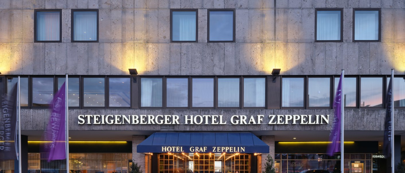 Außenansicht des Steigenberger Hotel Graf Zeppelin mit beleuchtetem Eingang und Fahnen., © Steigenberger Graf Zeppelin