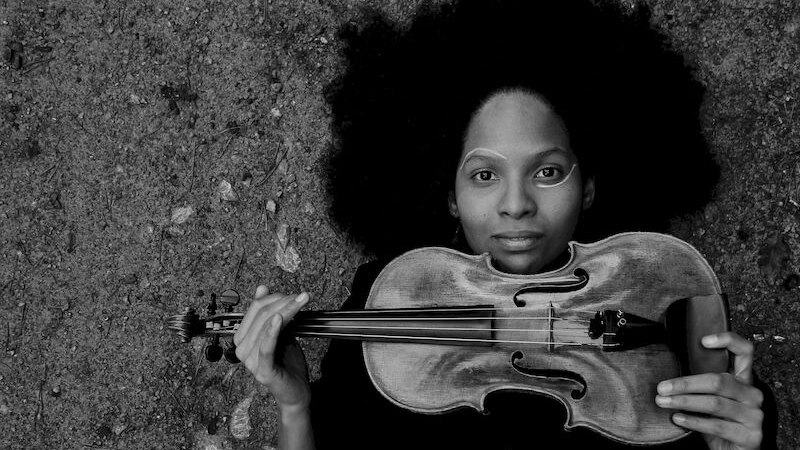 Person mit Afrofrisur liegt auf dem Boden und hält eine Geige. Schwarz-weiß Fotografie mit märchenhaftem Titel., © Stadt Sindelfingen Person mit Afrofrisur liegt auf dem Boden und hält eine Geige. Schwarz-weiß Fotografie mit märchenhaftem Titel., © Stadt Sindelfingen
