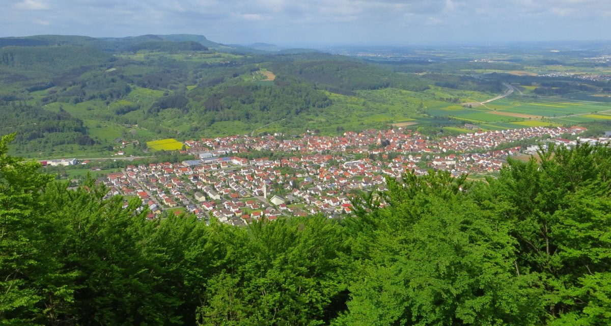 Panoramablick auf eine Stadt mit roten Dächern, umgeben von grünen Hügeln und Wäldern unter einem bewölkten Himmel., © Landkreis Göppingen Panoramablick auf eine Stadt mit roten Dächern, umgeben von grünen Hügeln und Wäldern unter einem bewölkten Himmel., © Landkreis Göppingen