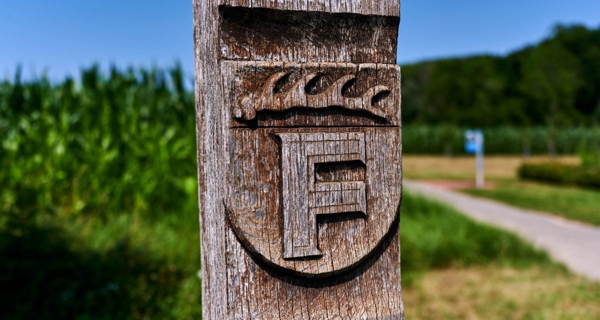 Holzpfosten mit geschnitztem Wappen und Buchstabe F, im Hintergrund ein Weg und gr&uuml;ne Landschaft., &copy; Kraichgau-Stromberg Tourismus e.V.