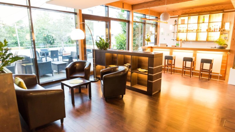 Moderne Hotel-Lounge mit Bar, Ledersesseln und großen Fenstern. Draußen ist eine Terrasse mit Sitzgelegenheiten sichtbar., © ARNOTEL GmbH Moderne Hotel-Lounge mit Bar, Ledersesseln und großen Fenstern. Draußen ist eine Terrasse mit Sitzgelegenheiten sichtbar., © ARNOTEL GmbH