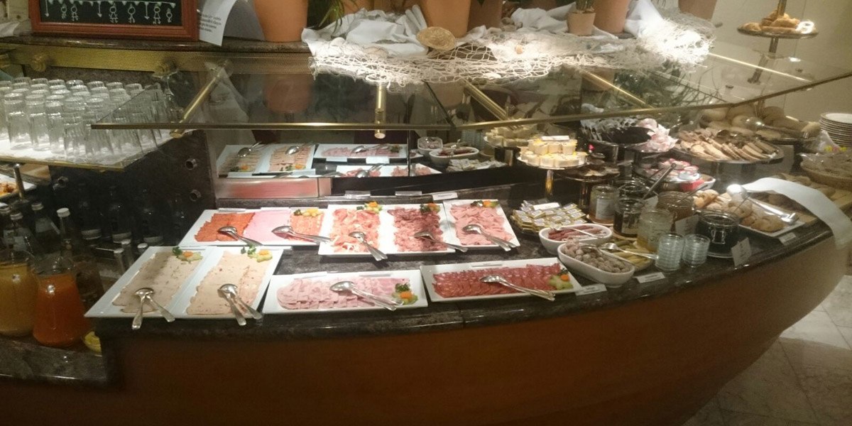 Ein Frühstücksbuffet mit verschiedenen Wurstsorten, Aufstrichen, Gläsern und Getränken. Im Hintergrund sind Brot und Gebäck zu sehen., © Hotel Unger