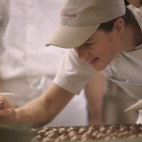 Eine Person in einer B&auml;ckerei verziert Pralinen mit einem Spritzbeutel. Sie tr&auml;gt eine Schirmm&uuml;tze und ein wei&szlig;es T-Shirt., &copy; Stadt G&ouml;ppingen