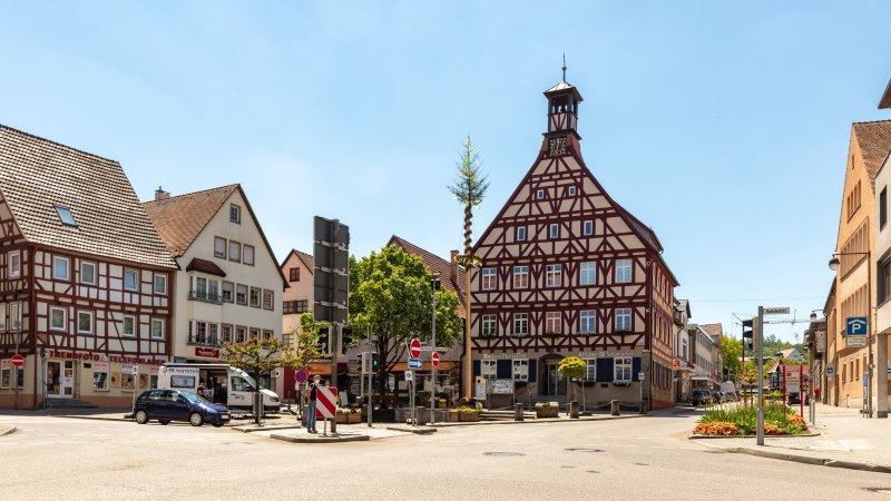 Platz ges&auml;umt von verschiedenen Geb&auml;uden, darunter zwei mit FAchwerkfassaden, in der Platzmitte Baum und Brunnen, &copy; Stadt Gaildorf
