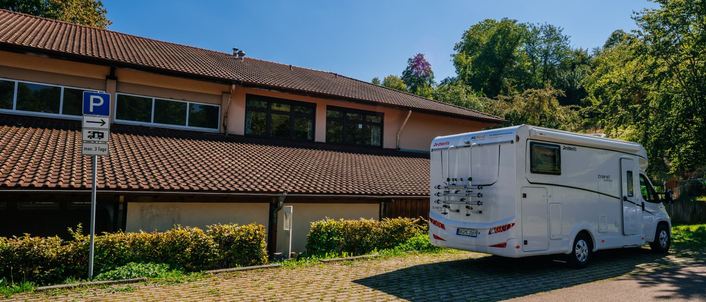 Wohnmobil auf einem Stellplatz neben einem Gebäude mit Ziegeldach, umgeben von Bäumen und einem blauen Himmel., © Stuttgart-Marketing GmbH, Thomas Niedermüller Wohnmobil auf einem Stellplatz neben einem Gebäude mit Ziegeldach, umgeben von Bäumen und einem blauen Himmel., © Stuttgart-Marketing GmbH, Thomas Niedermüller