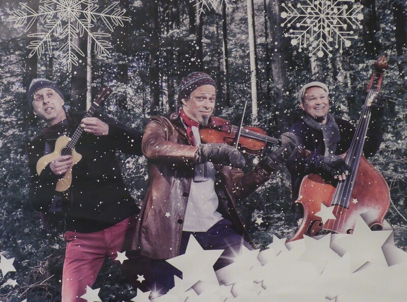Drei Musiker im Wald, umgeben von Schneeflocken und Sternen, spielen Ukulele, Geige und Kontrabass. Winterliche Atmosphäre., © Mauerwerk GmbH