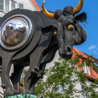 Surreale Kuhskulptur mit metallischem Bauch und goldenen Hörnern vor einem Gebäude mit roten Dachziegeln., © Stuttgart-Marketing GmbH Surreale Kuhskulptur mit metallischem Bauch und goldenen Hörnern vor einem Gebäude mit roten Dachziegeln., © Stuttgart-Marketing GmbH