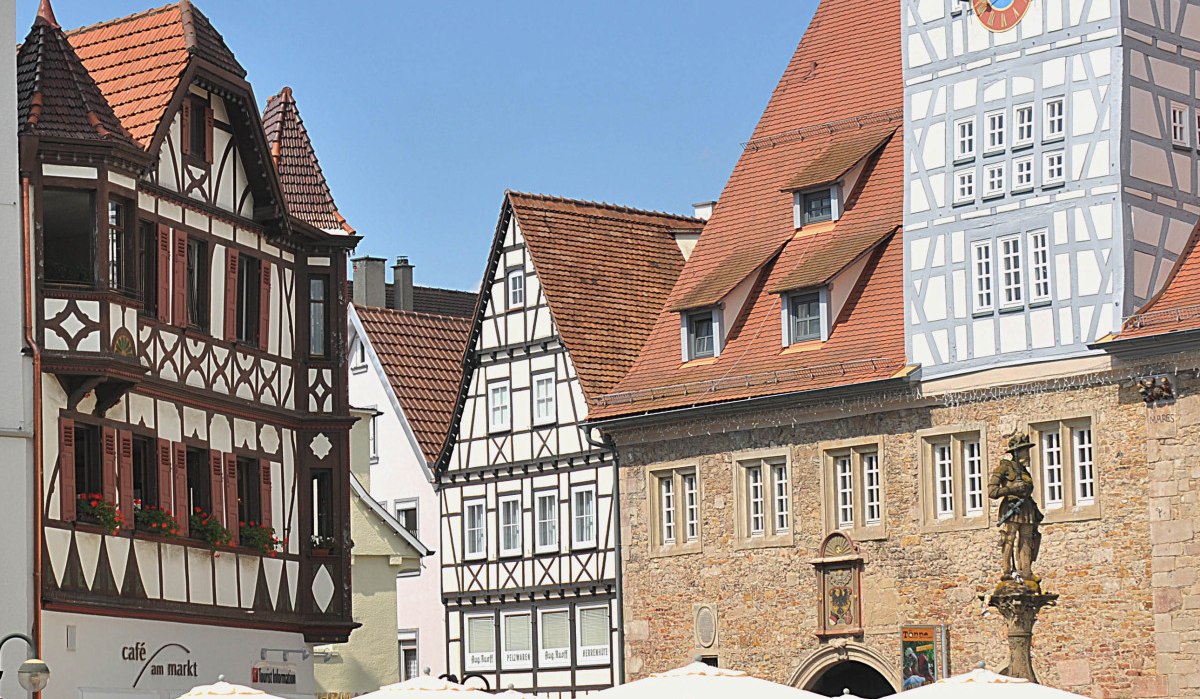 Reutlinger Marktplatz mit Fachwerkhäusern, Menschen sitzen in einem Straßencafé unter Sonnenschirmen, blauer Himmel., © Mythos Schwäbische Alb im Landkreis Reutlingen e.V.
