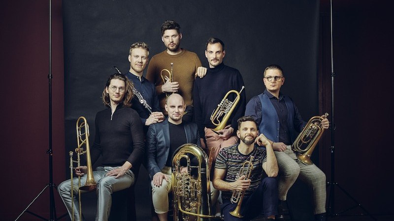 Sieben Männer mit Blasinstrumenten posieren vor einem dunklen Hintergrund. Sie tragen lässige, moderne Kleidung und blicken in die Kamera., © Stadtverwaltung Vaihingen an der Enz Sieben Männer mit Blasinstrumenten posieren vor einem dunklen Hintergrund. Sie tragen lässige, moderne Kleidung und blicken in die Kamera., © Stadtverwaltung Vaihingen an der Enz