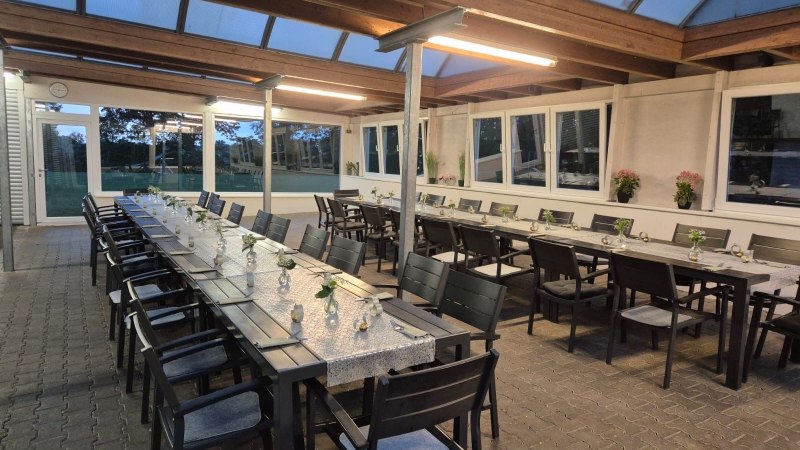 Ein &uuml;berdachter Au&szlig;enbereich mit langen, gedeckten Tischen und St&uuml;hlen, dekoriert mit kleinen Blumenvasen. Die Umgebung wirkt einladend und modern., &copy; Restaurant Lingam