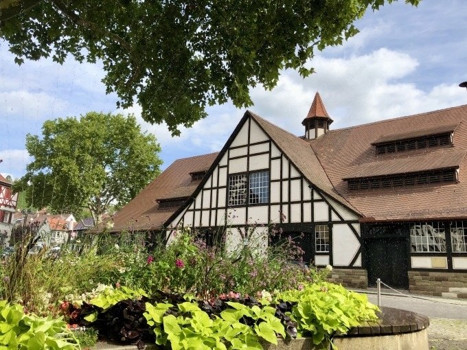 Fachwerkgeb&auml;ude mit rotem Dach, umgeben von B&auml;umen und Blumenbeet im Vordergrund. Klarer Himmel und sonniges Wetter., &copy; Stuttgart Marketing GmbH