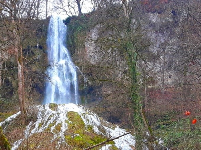 Ein hoher Wasserfall flie&szlig;t &uuml;ber eine Felswand, umgeben von kahlen B&auml;umen und Moos im Wald., &copy; SwabianTravel