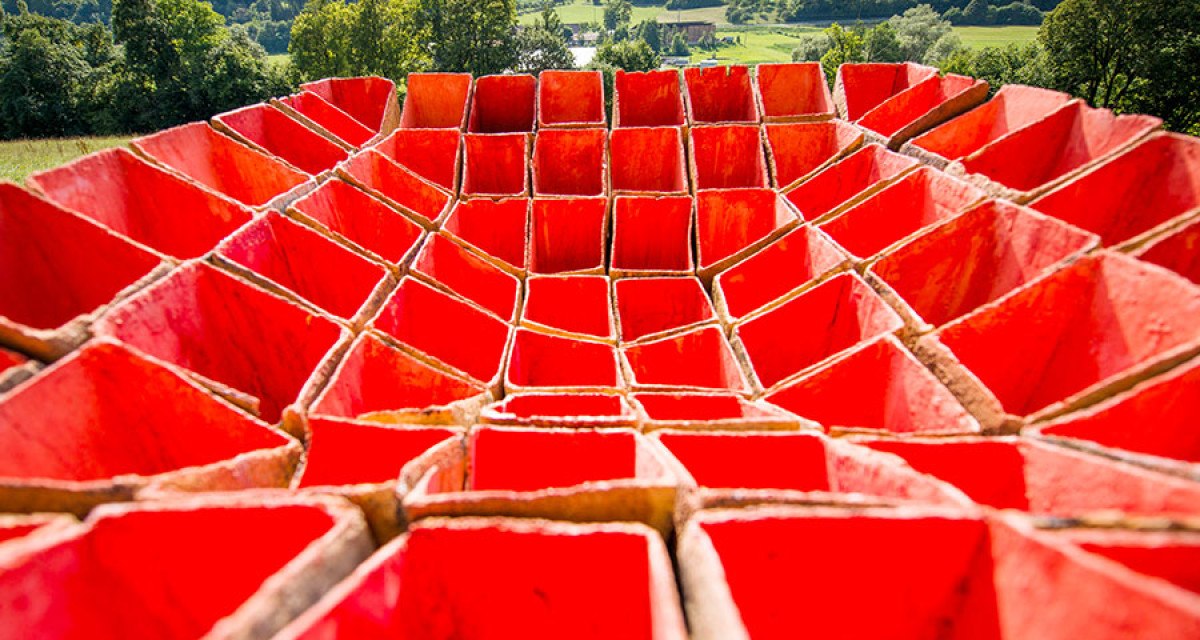 Rote, geometrische Struktur in Form eines Kraters vor einer grünen Landschaft mit Bäumen und Hügeln im Hintergrund., © Natur.Nah. Schönbuch & Heckengäu