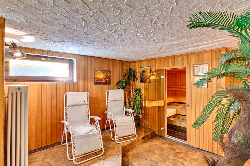Ein gemütlicher Saunaraum mit zwei weißen Liegestühlen, Holzwänden, Pflanzen und einer kleinen Sauna im Hintergrund., © Römerhof Hotelbetriebs GmbH